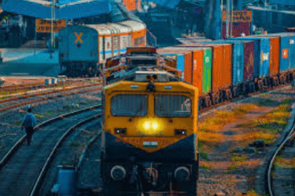 A freight train passing through a cargo terminal under the Gati Shakti initiative, showcasing multiple loading bays, containers, and cargo handling equipment.