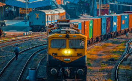 A freight train passing through a cargo terminal under the Gati Shakti initiative, showcasing multiple loading bays, containers, and cargo handling equipment.